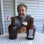 Photo of Great British Pub Crawls Guide Mike holding a glass of beer with two oversize bottles of beer in foreground